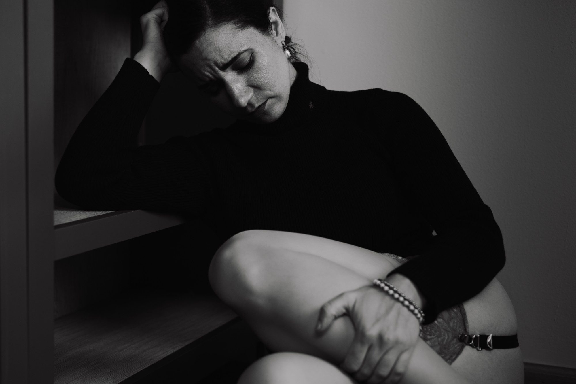 Black and white portrait of a woman in a black turtleneck sitting on a staircase, eyes closed, head resting on her hand